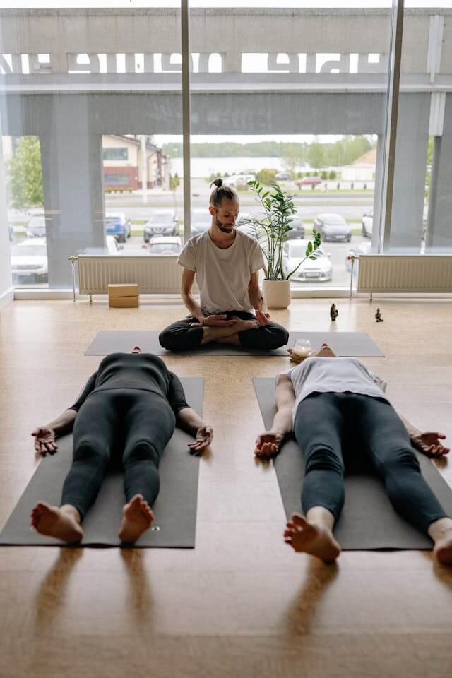 yoga teacher in studio with couple lying on mat in corpse pose